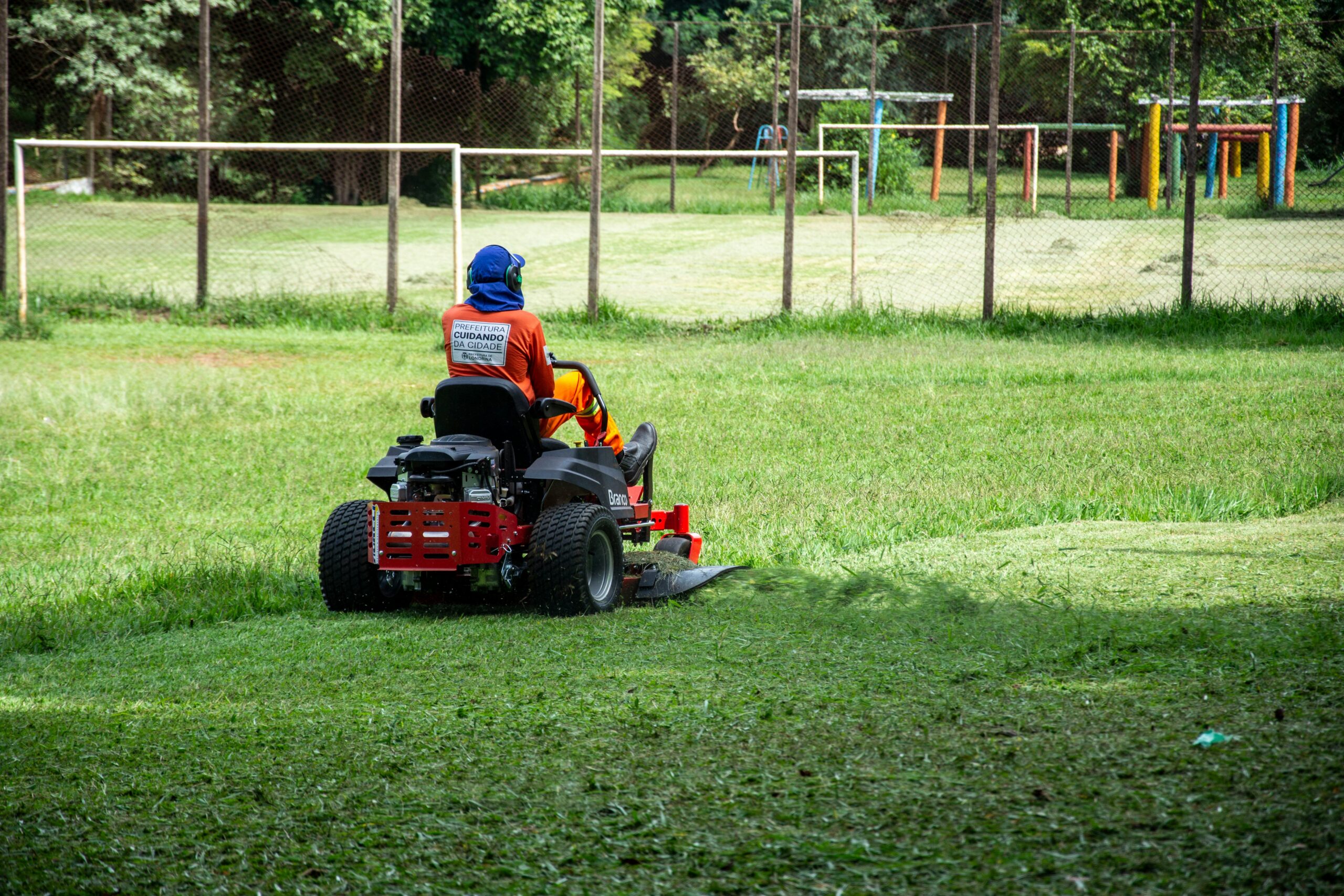 Individual operating a riding lawnmower on a grassy field in a recreational park, Londrina, Brazil.